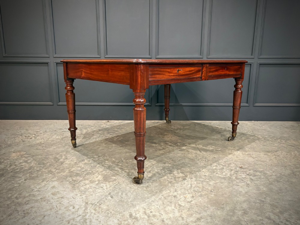 A rectangular Cuban mahogany library writing table featuring a polished wood top, frieze drawers with small keyholes, and turned legs with brass castors. View II