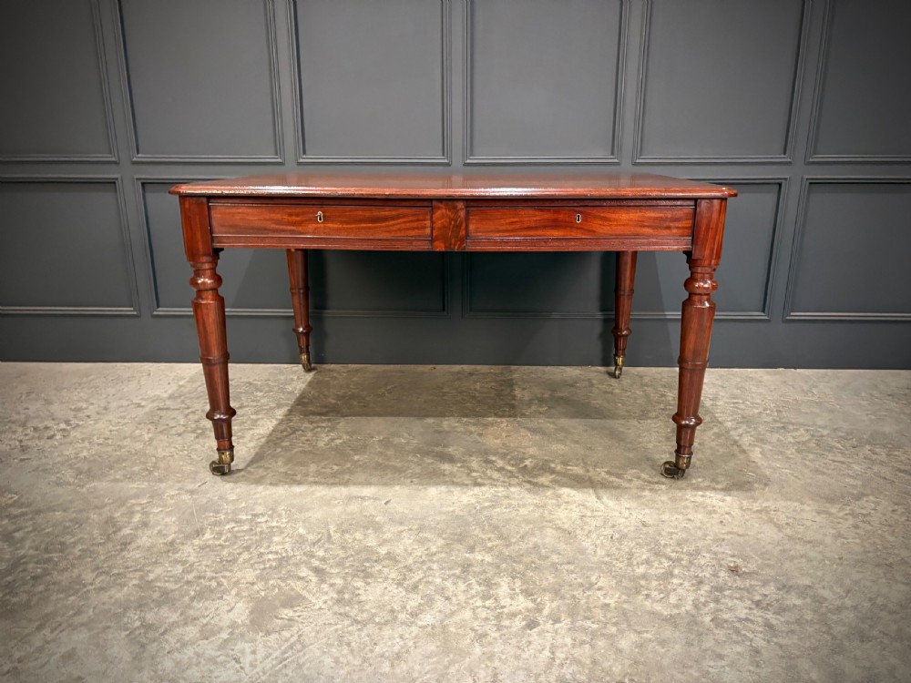 A rectangular Cuban mahogany library writing table featuring a polished wood top, frieze drawers with small keyholes, and turned legs with brass castors. View V