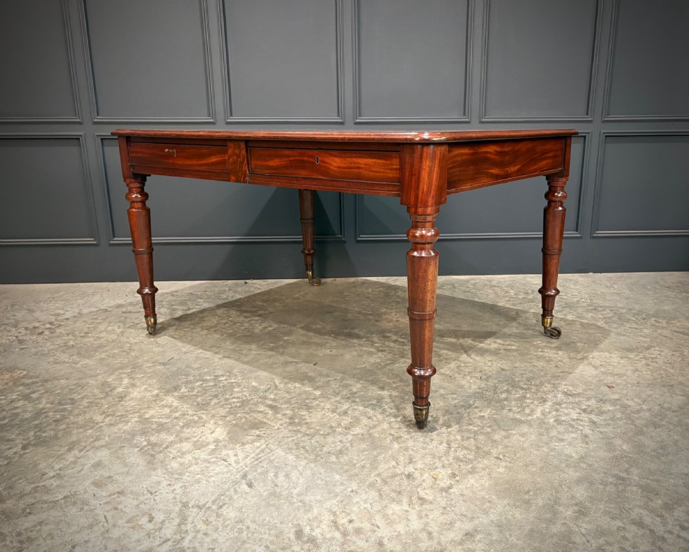 A rectangular Cuban mahogany library writing table featuring a polished wood top, frieze drawers with small keyholes, and turned legs with brass castors. View VIII