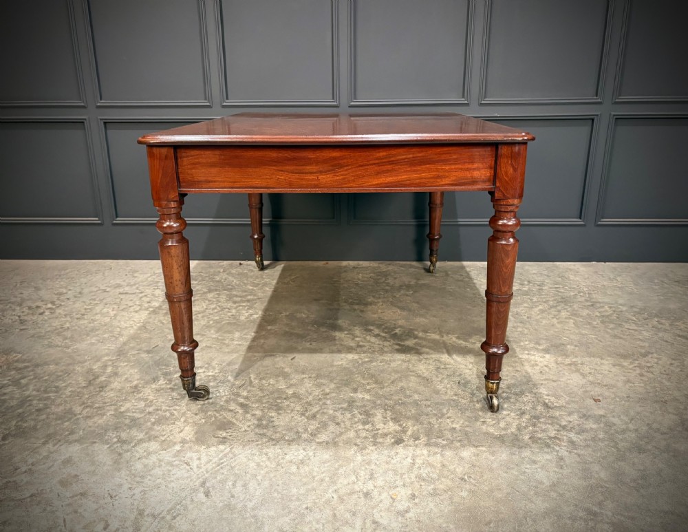 A rectangular Cuban mahogany library writing table featuring a polished wood top, frieze drawers with small keyholes, and turned legs with brass castors. View XI