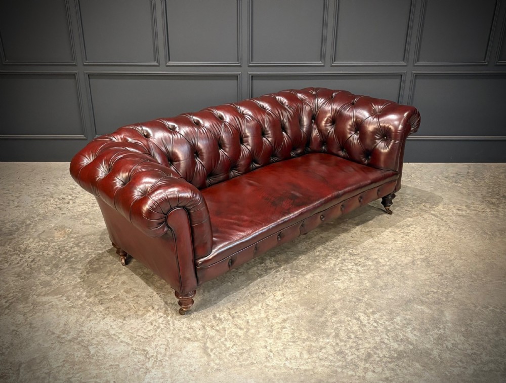 A Victorian oxblood leather Chesterfield sofa featuring deep buttoned upholstery, rolled arms, and turned wooden legs with brass castors.