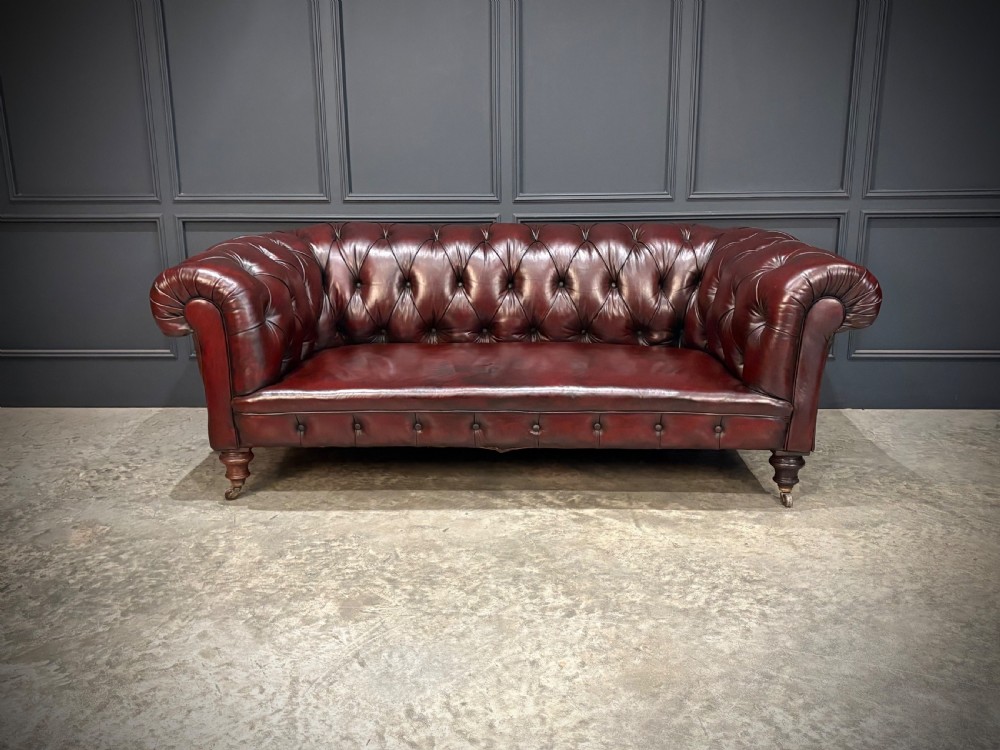 A Victorian oxblood leather Chesterfield sofa featuring deep buttoned upholstery, rolled arms, and turned wooden legs with brass castors. View V