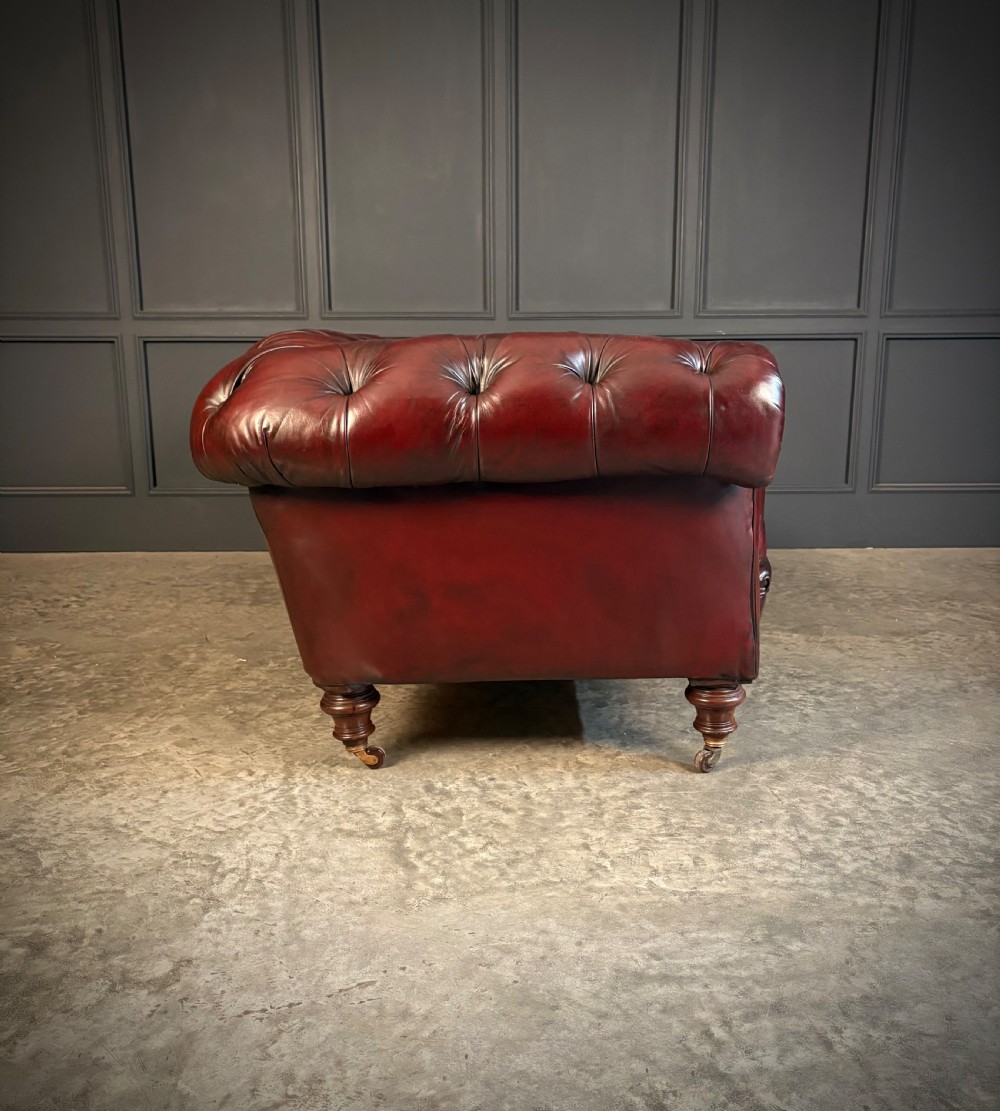 A Victorian oxblood leather Chesterfield sofa featuring deep buttoned upholstery, rolled arms, and turned wooden legs with brass castors. View VIII