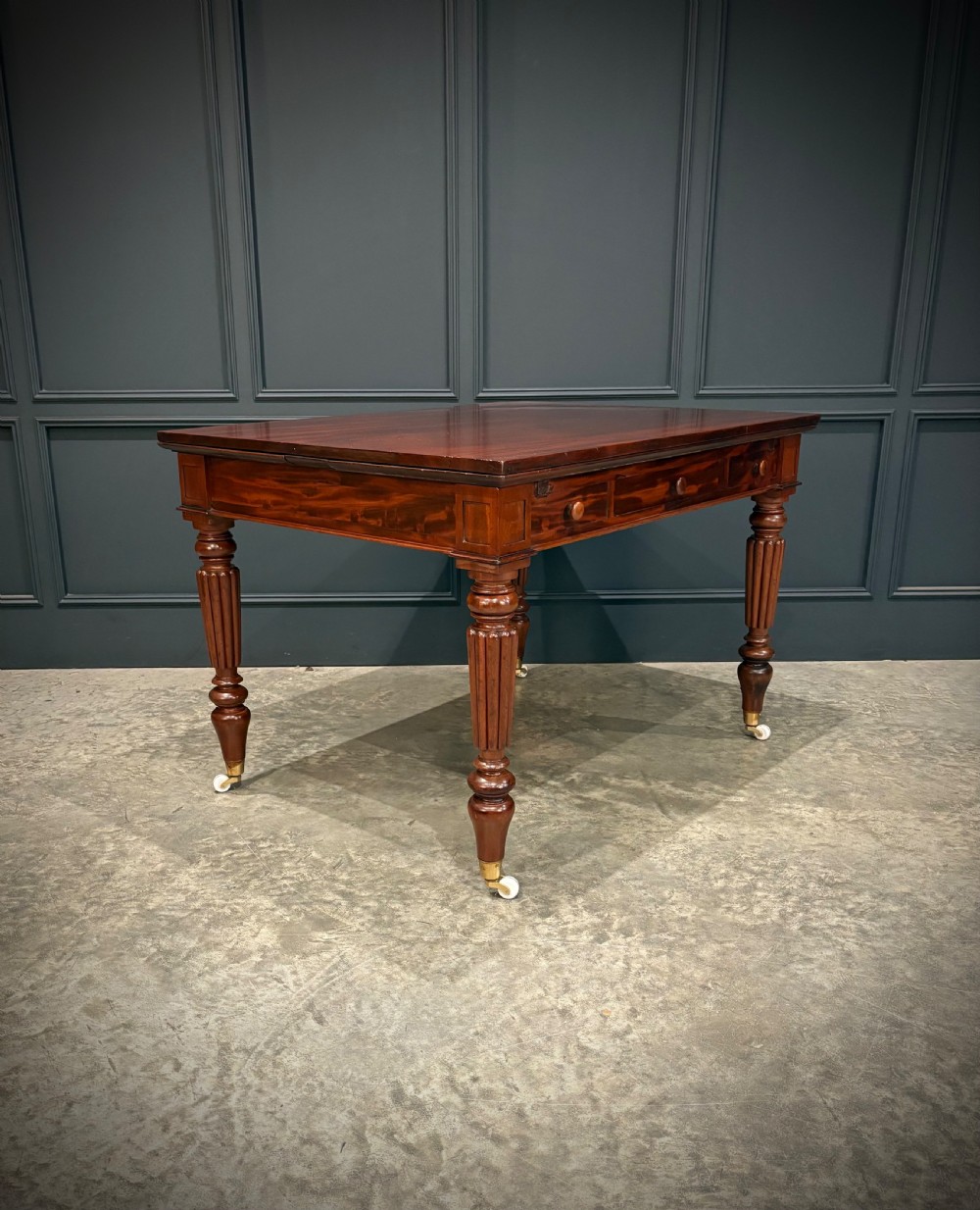 Victorian mahogany writing table with a polished flat top, frieze drawers with wooden turned knobs, and reeded turned legs on brass castors. View II