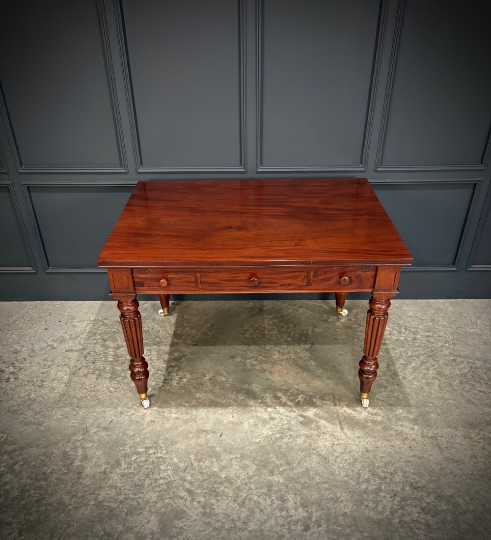 Victorian mahogany writing table with a polished flat top, frieze drawers with wooden turned knobs, and reeded turned legs on brass castors.