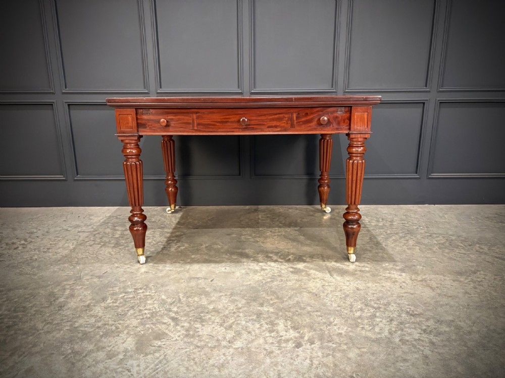 Victorian mahogany writing table with a polished flat top, frieze drawers with wooden turned knobs, and reeded turned legs on brass castors. View VI