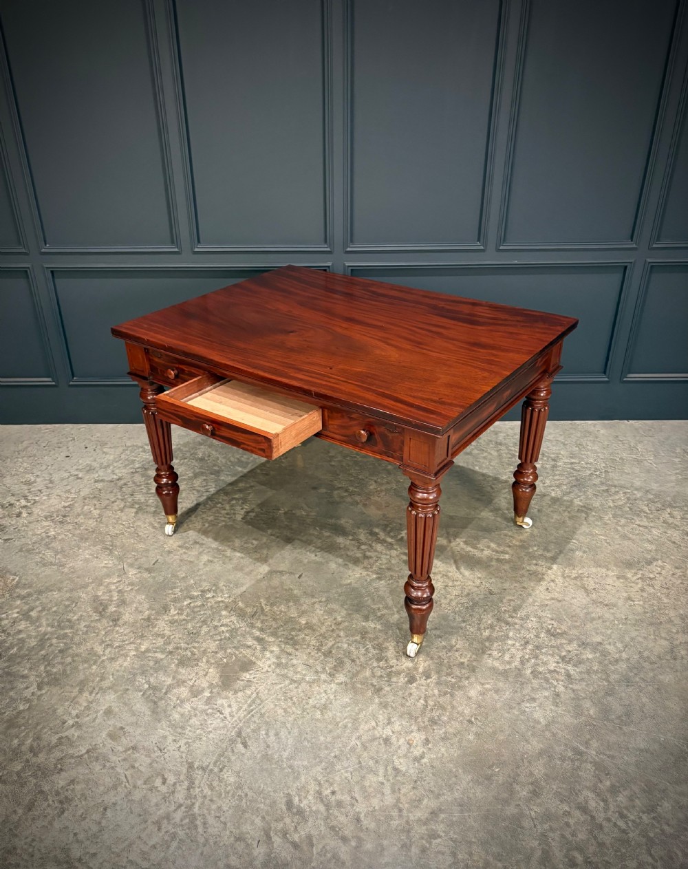 Victorian mahogany writing table with a polished flat top, frieze drawers with wooden turned knobs, and reeded turned legs on brass castors. View IX