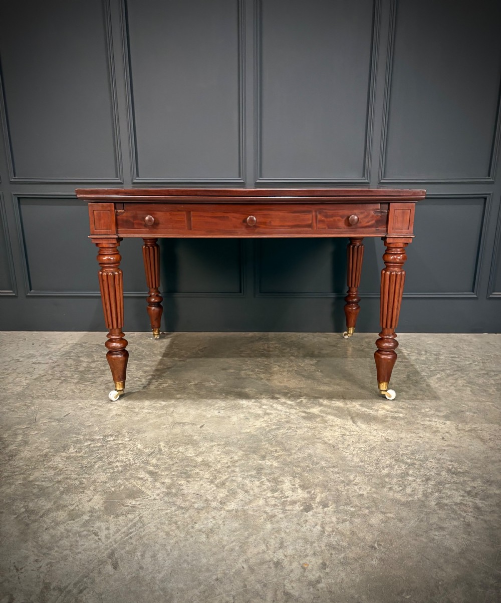 Victorian mahogany writing table with a polished flat top, frieze drawers with wooden turned knobs, and reeded turned legs on brass castors. View XII