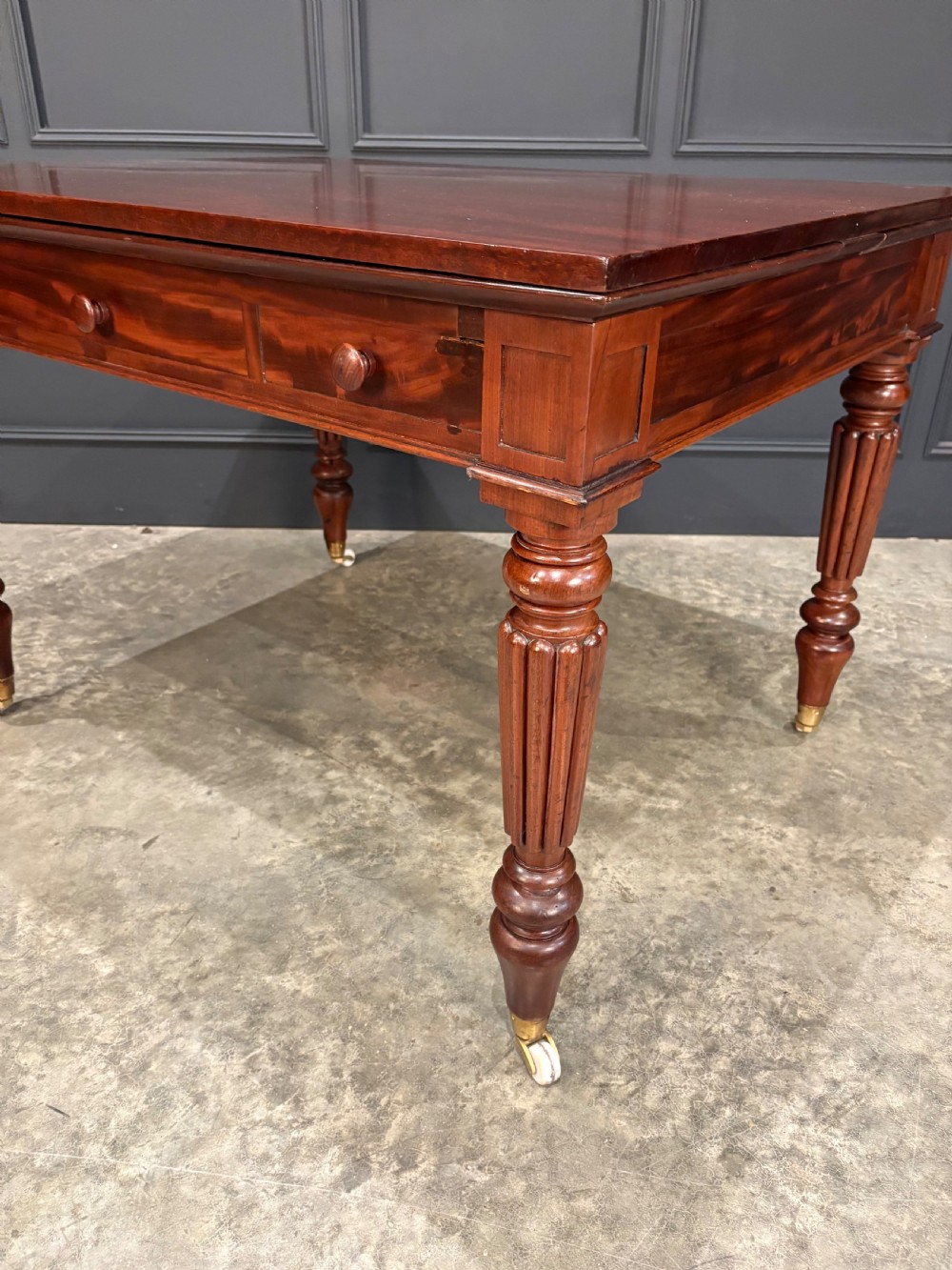 Victorian mahogany writing table with a polished flat top, frieze drawers with wooden turned knobs, and reeded turned legs on brass castors. View XIII