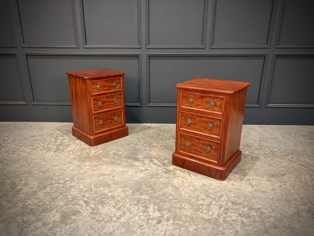A pair of Victorian mahogany bedside chests, each featuring three drawers with brass drop ring handles on a solid plinth base.