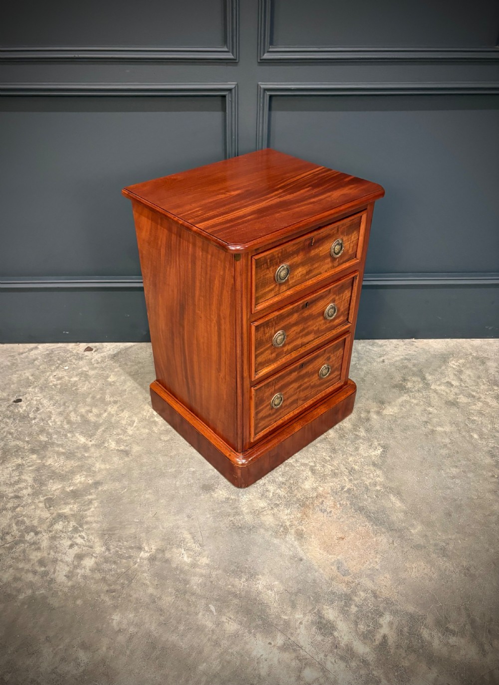A pair of Victorian mahogany bedside chests, each featuring three drawers with brass drop ring handles on a solid plinth base. View IV
