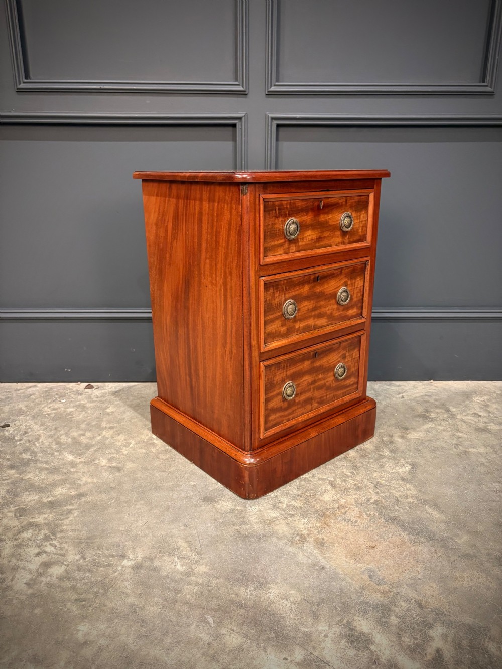 A pair of Victorian mahogany bedside chests, each featuring three drawers with brass drop ring handles on a solid plinth base. View V