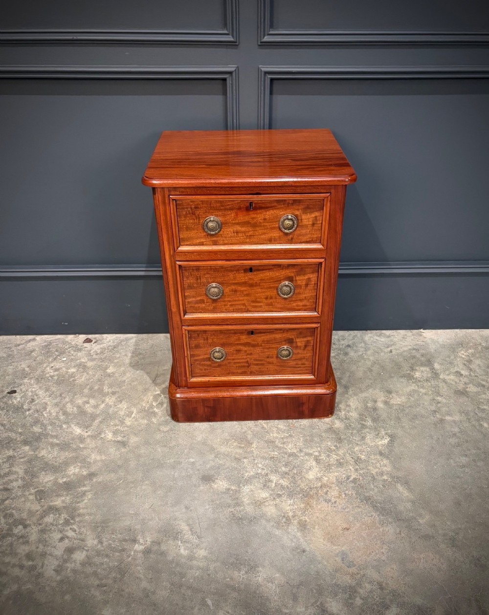 A pair of Victorian mahogany bedside chests, each featuring three drawers with brass drop ring handles on a solid plinth base. View VI