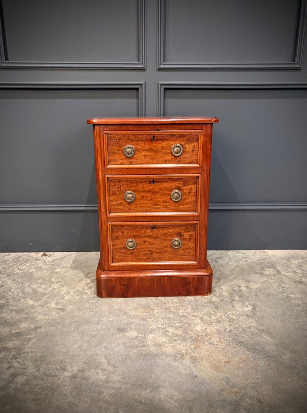 A pair of Victorian mahogany bedside chests, each featuring three drawers with brass drop ring handles on a solid plinth base. View VII