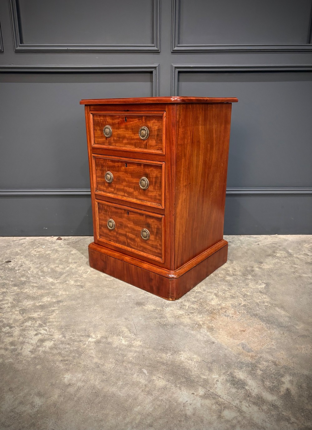 A pair of Victorian mahogany bedside chests, each featuring three drawers with brass drop ring handles on a solid plinth base. View IX