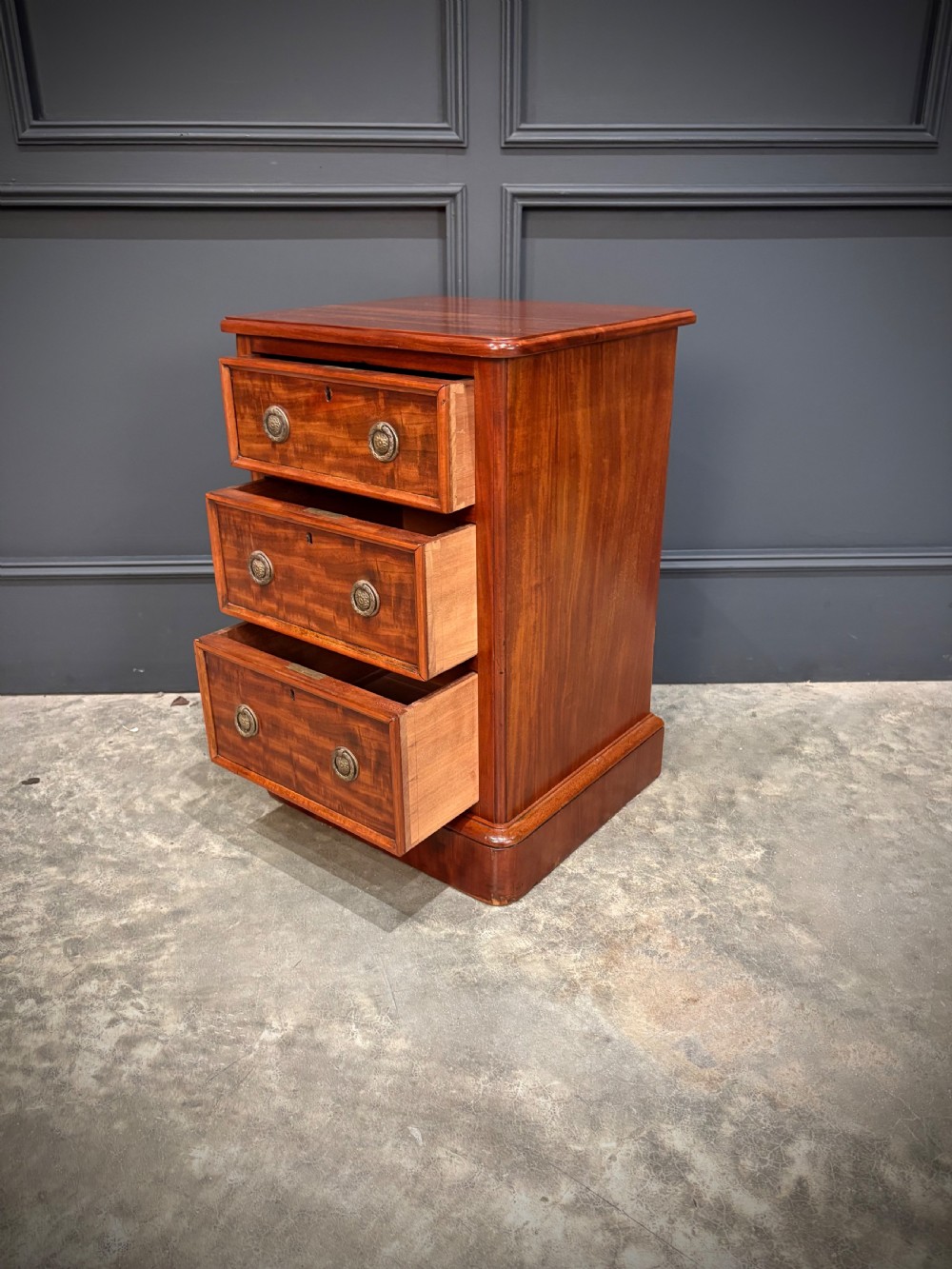 A pair of Victorian mahogany bedside chests, each featuring three drawers with brass drop ring handles on a solid plinth base. View X