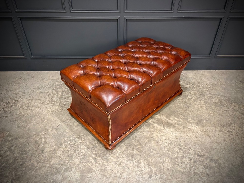 A large Regency style chestnut brown leather storage ottoman featuring deep diamond button tufting and brass stud trim on a shaped base.