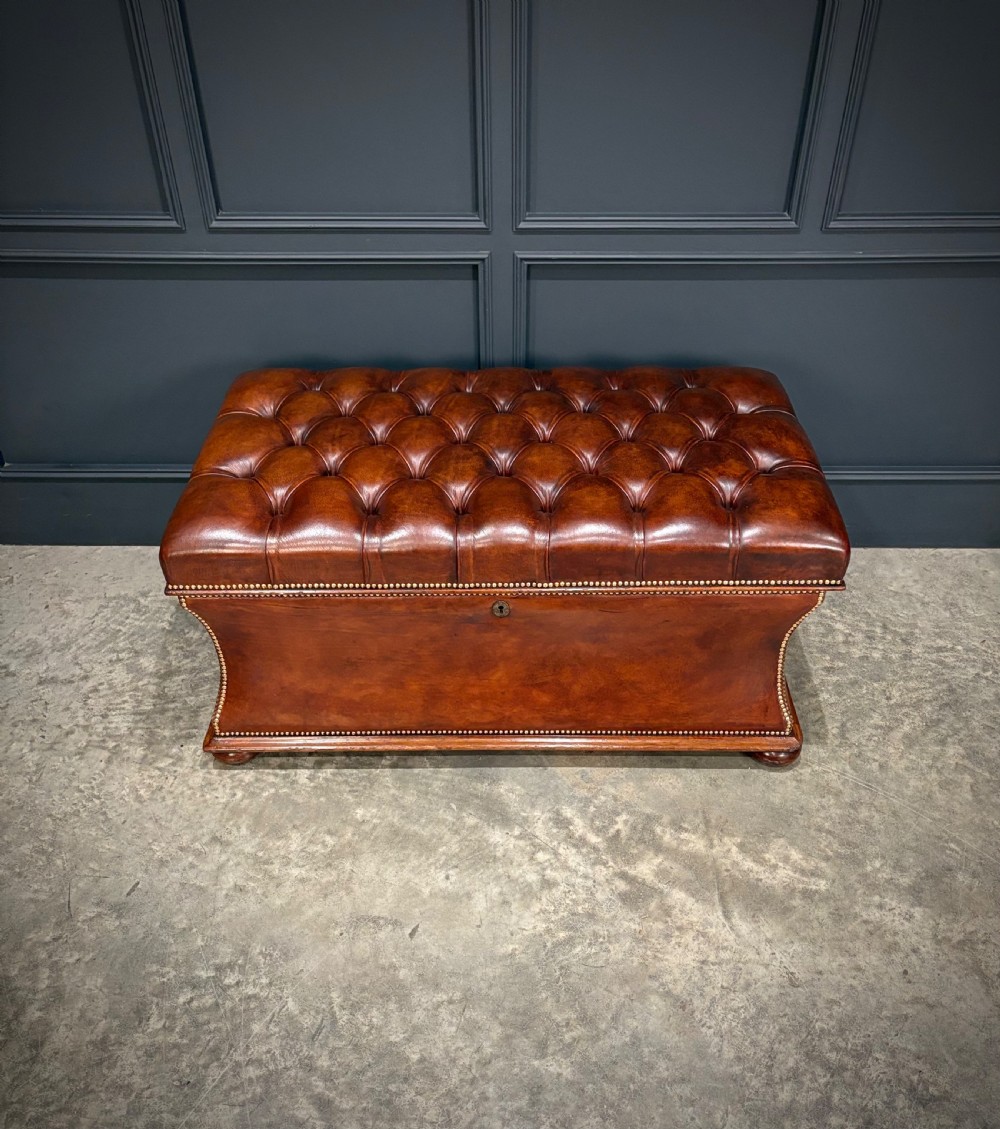 A large Regency style chestnut brown leather storage ottoman featuring deep diamond button tufting and brass stud trim on a shaped base. View III