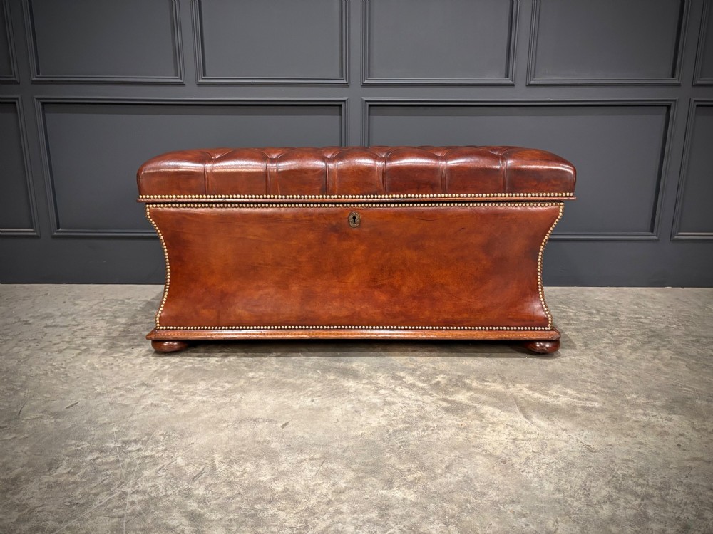 A large Regency style chestnut brown leather storage ottoman featuring deep diamond button tufting and brass stud trim on a shaped base. View IV