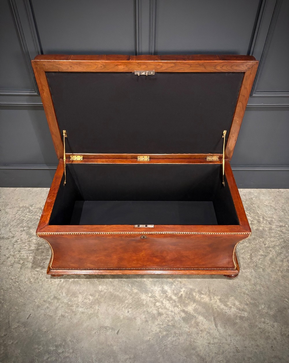 A large Regency style chestnut brown leather storage ottoman featuring deep diamond button tufting and brass stud trim on a shaped base. View V