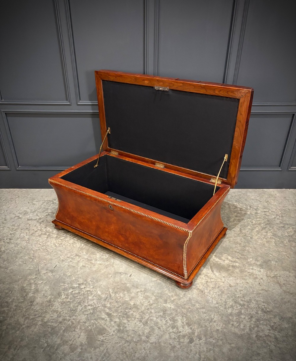 A large Regency style chestnut brown leather storage ottoman featuring deep diamond button tufting and brass stud trim on a shaped base. View VI