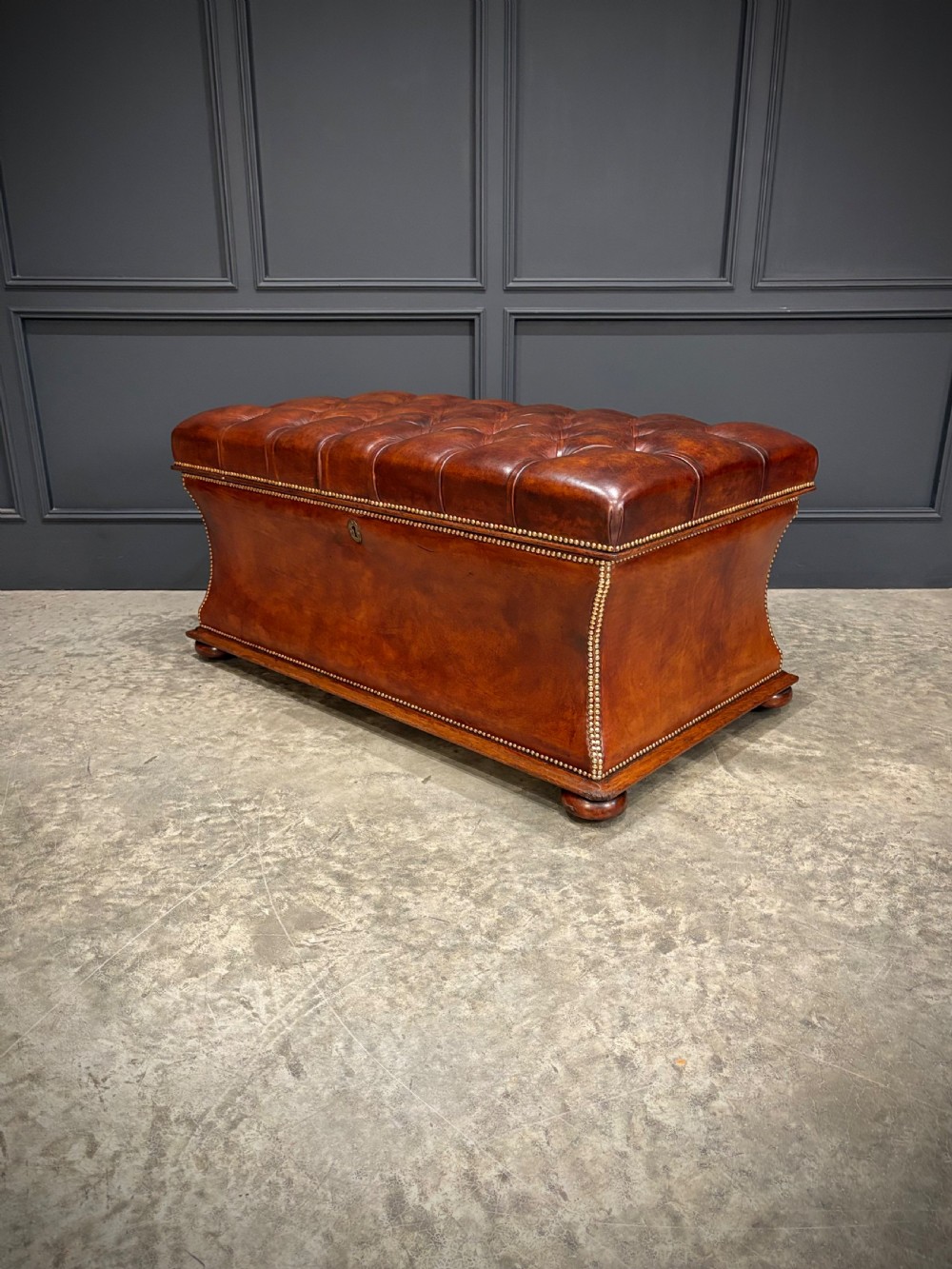 A large Regency style chestnut brown leather storage ottoman featuring deep diamond button tufting and brass stud trim on a shaped base. View VIII