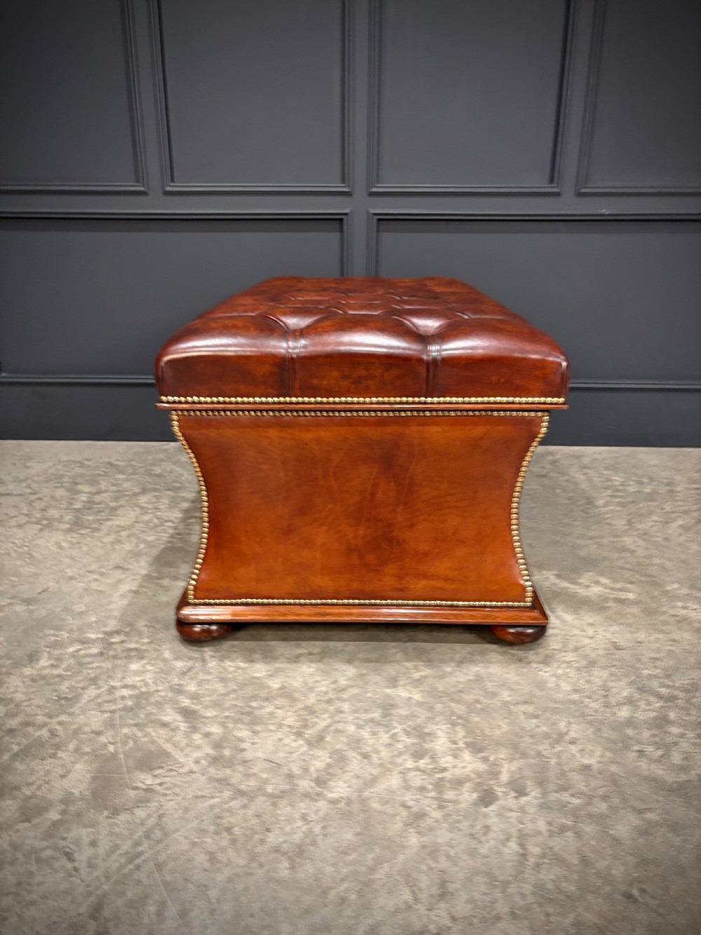 A large Regency style chestnut brown leather storage ottoman featuring deep diamond button tufting and brass stud trim on a shaped base. View IX