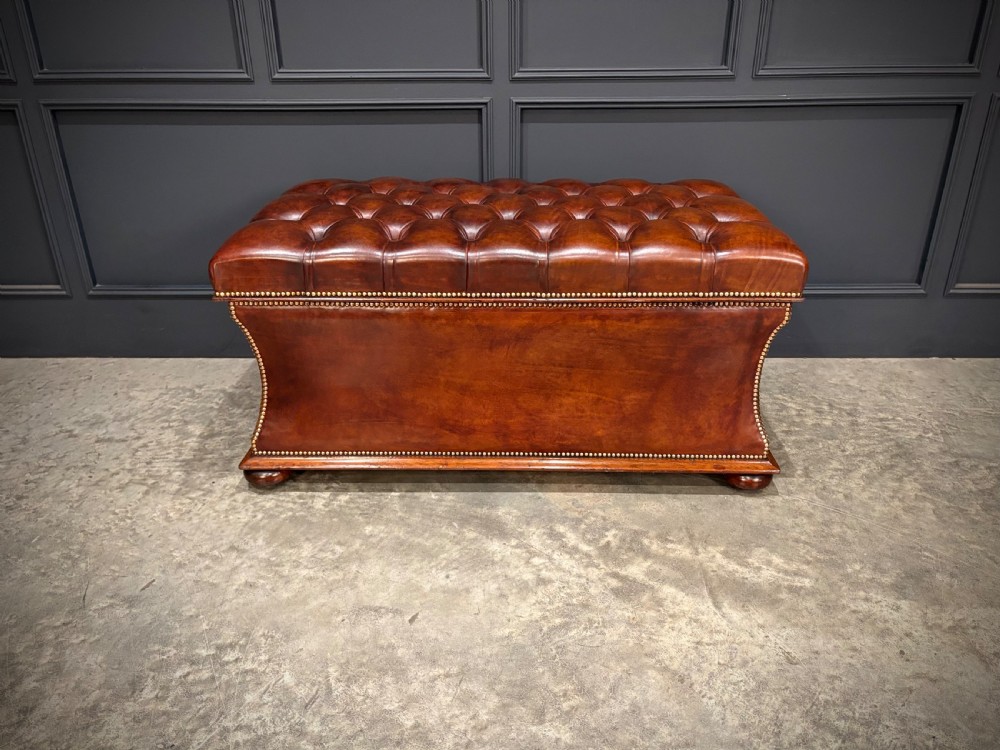 A large Regency style chestnut brown leather storage ottoman featuring deep diamond button tufting and brass stud trim on a shaped base. View X
