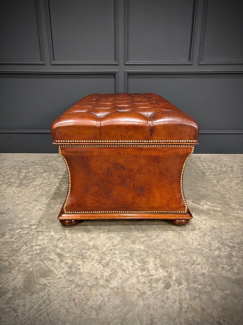 A large Regency style chestnut brown leather storage ottoman featuring deep diamond button tufting and brass stud trim on a shaped base. View XI