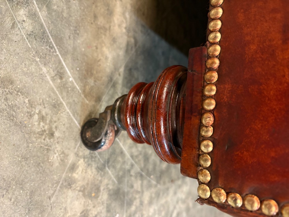 A large Victorian Chesterfield sofa featuring deep buttoned chestnut brown leather upholstery, rolled arms, brass stud detailing, and turned legs on castors. View XI