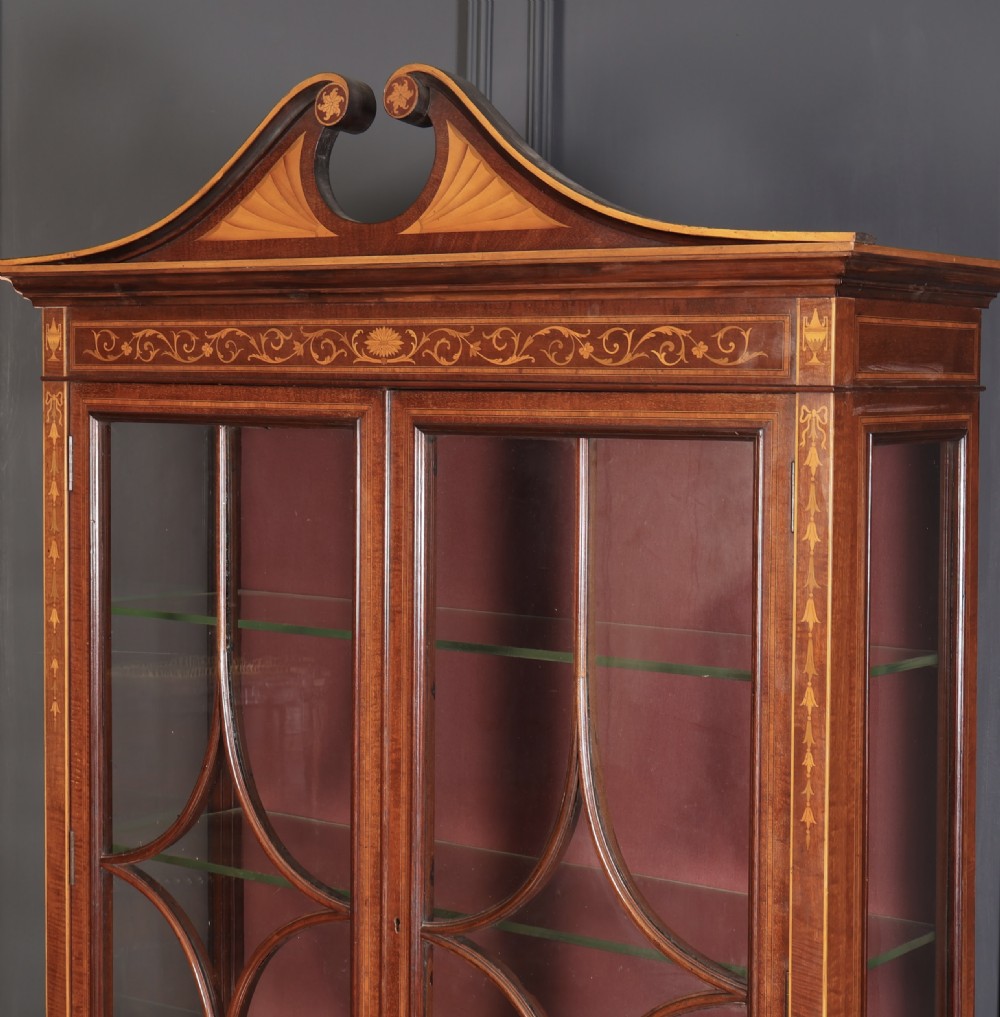 A tall mahogany glazed cabinet bookcase featuring marquetry inlay, astragal glazed doors, a swan-neck pediment, and a two-door lower cupboard. View VII