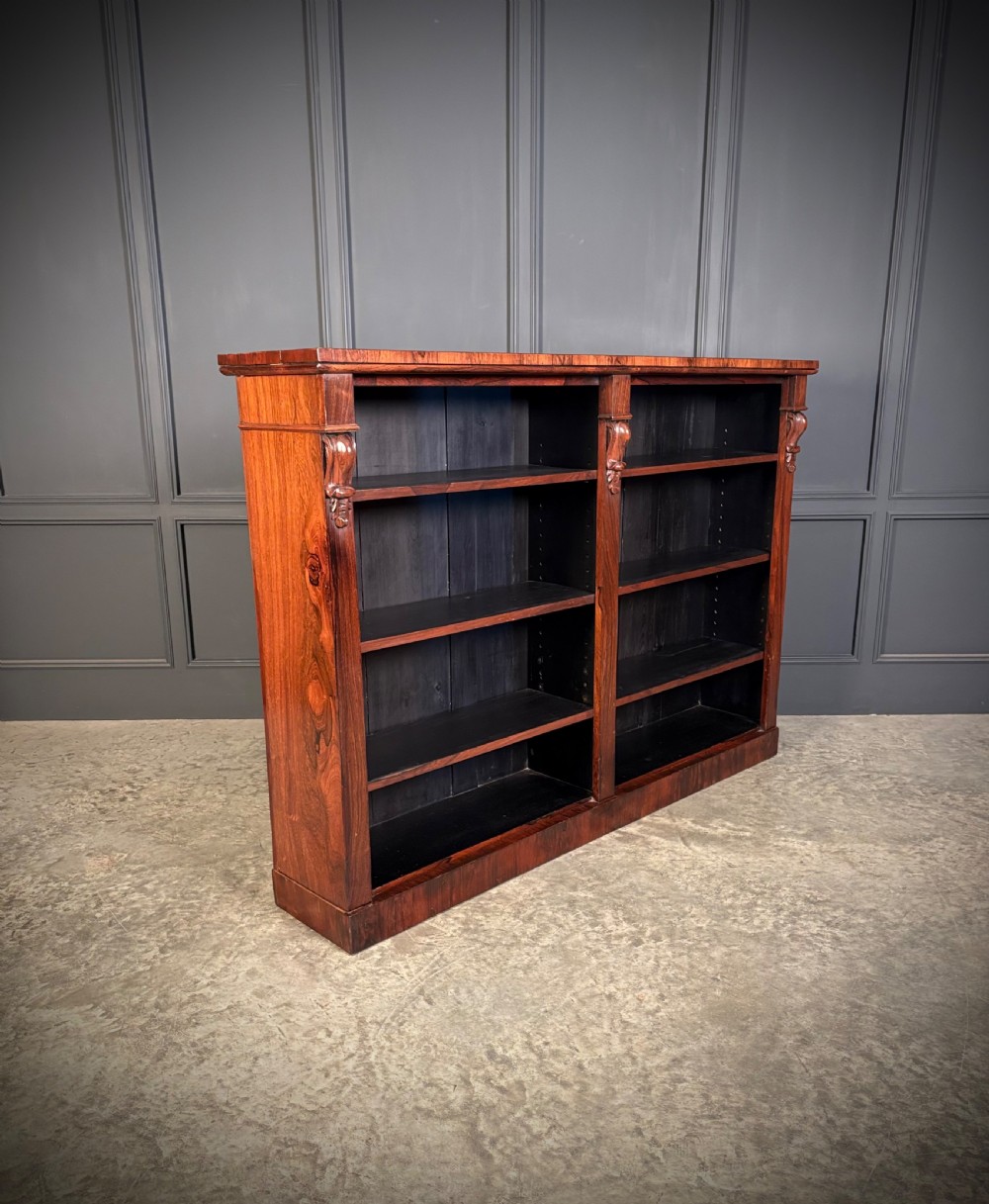 A low Victorian open bookcase made from dark rosewood with two bays of adjustable shelves and carved corbels. View II