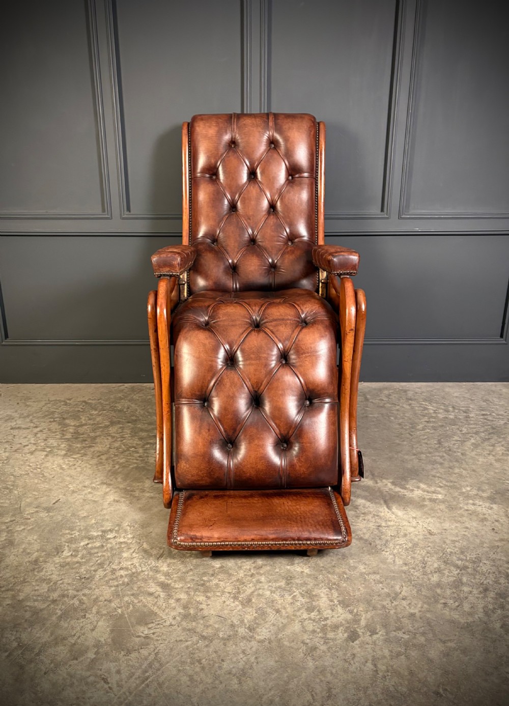 A Regency mahogany reclining armchair featuring button-tufted brown leather upholstery, padded armrests, an adjustable footrest, brass castors, and carved timber details. View III