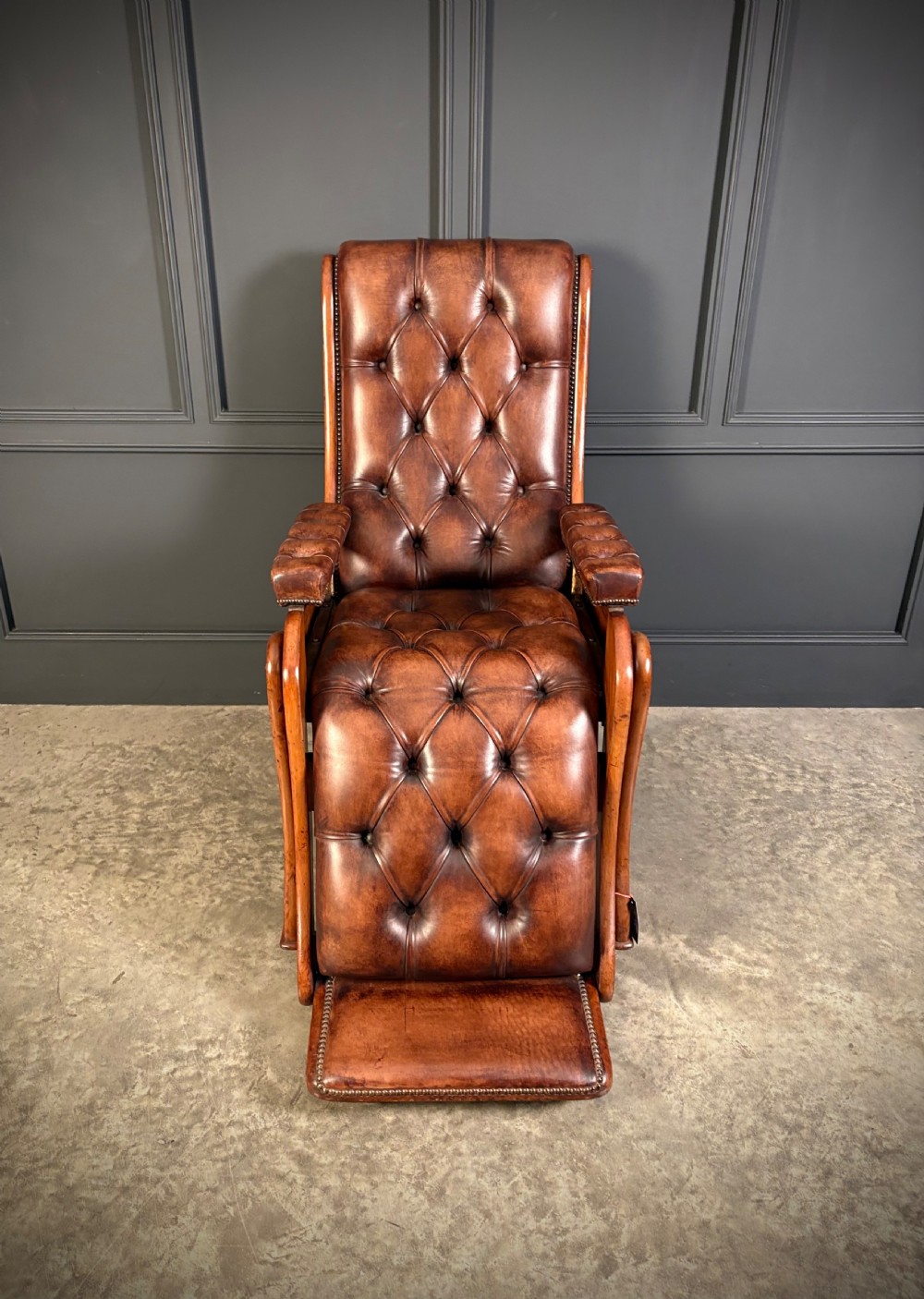 A Regency mahogany reclining armchair featuring button-tufted brown leather upholstery, padded armrests, an adjustable footrest, brass castors, and carved timber details. View IV
