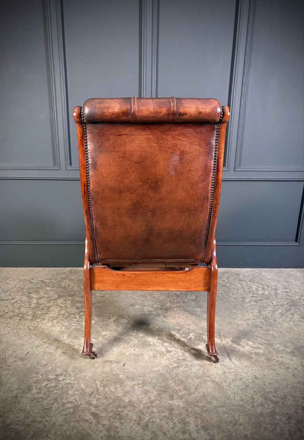 A Regency mahogany reclining armchair featuring button-tufted brown leather upholstery, padded armrests, an adjustable footrest, brass castors, and carved timber details. View XII
