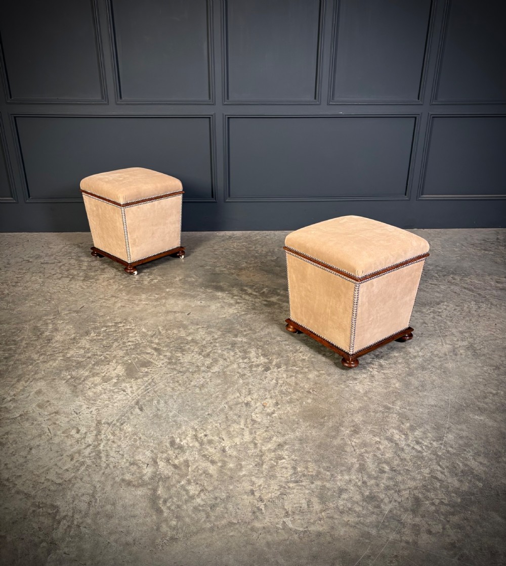 A pair of square Regency style ottomans upholstered in beige fabric with brass stud trimming, raised on short mahogany legs with castors. View III