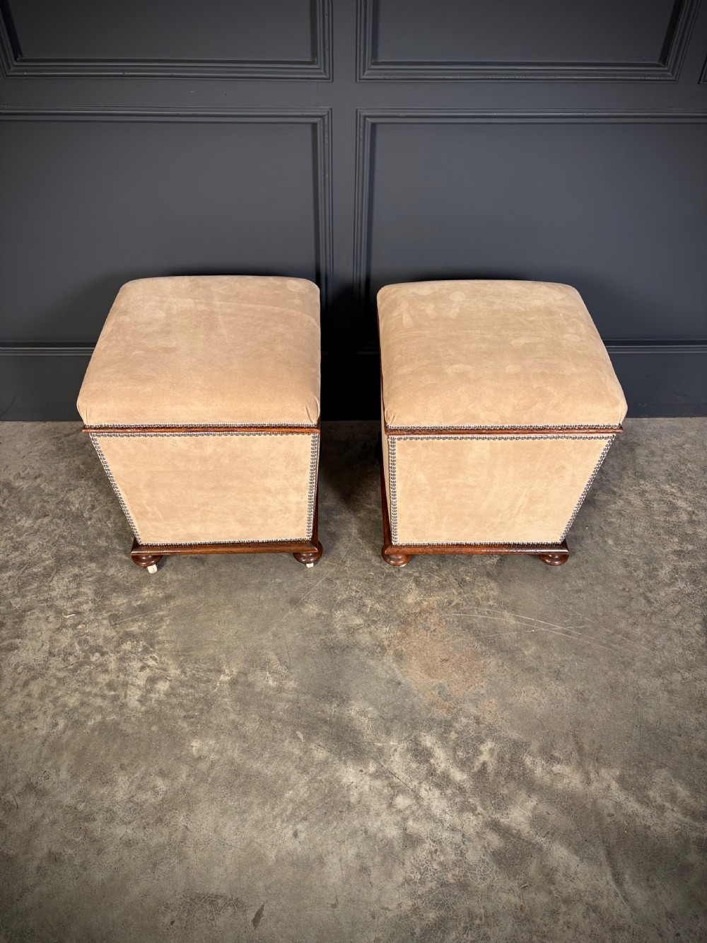 A pair of square Regency style ottomans upholstered in beige fabric with brass stud trimming, raised on short mahogany legs with castors. View IV