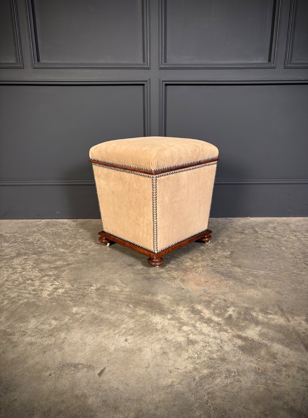 A pair of square Regency style ottomans upholstered in beige fabric with brass stud trimming, raised on short mahogany legs with castors. View V