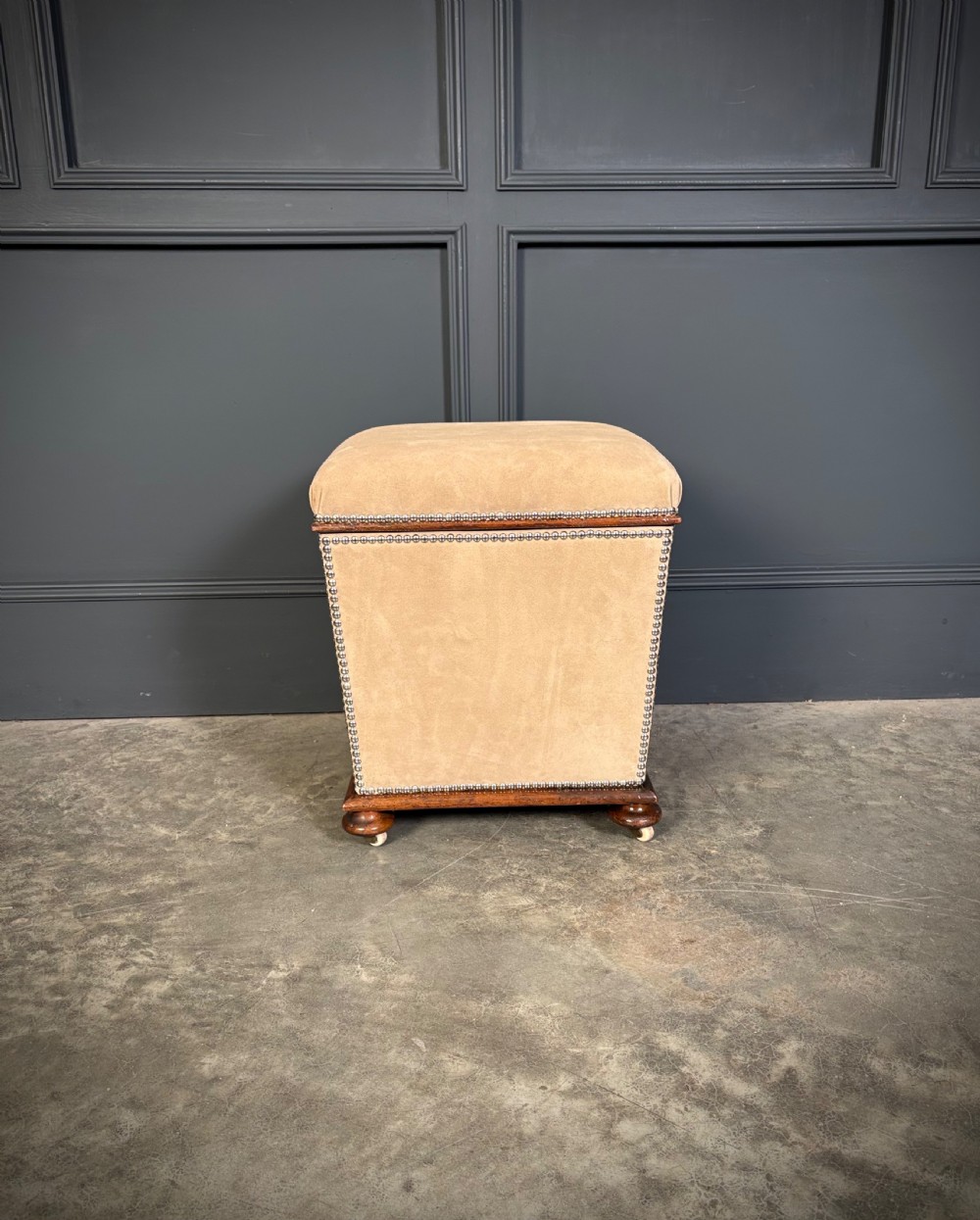 A pair of square Regency style ottomans upholstered in beige fabric with brass stud trimming, raised on short mahogany legs with castors. View VI