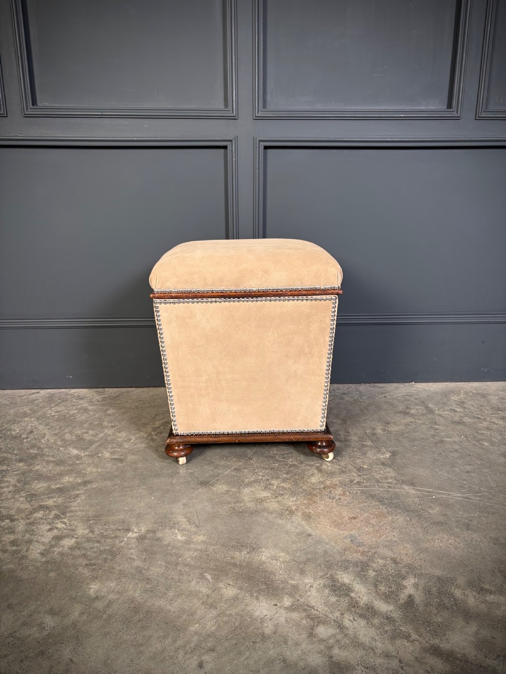 A pair of square Regency style ottomans upholstered in beige fabric with brass stud trimming, raised on short mahogany legs with castors. View X