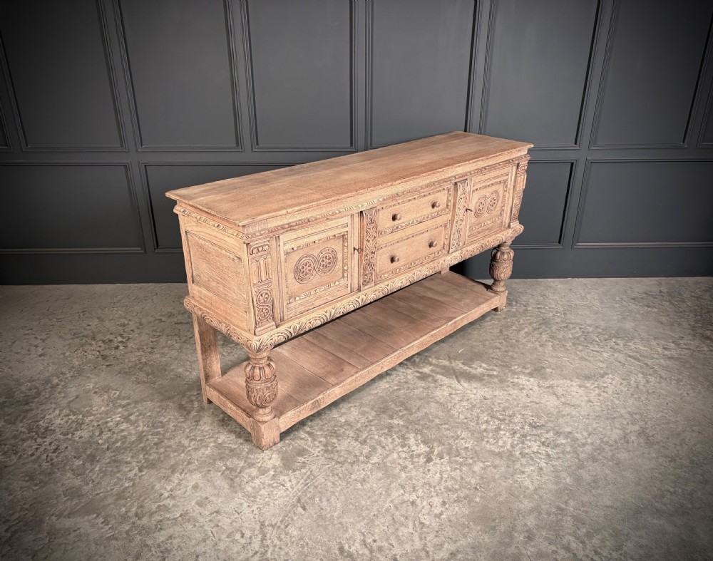 A carved bleached oak sideboard featuring geometric relief panel doors, central drawers, turned front legs, and an open lower pot board shelf. View II