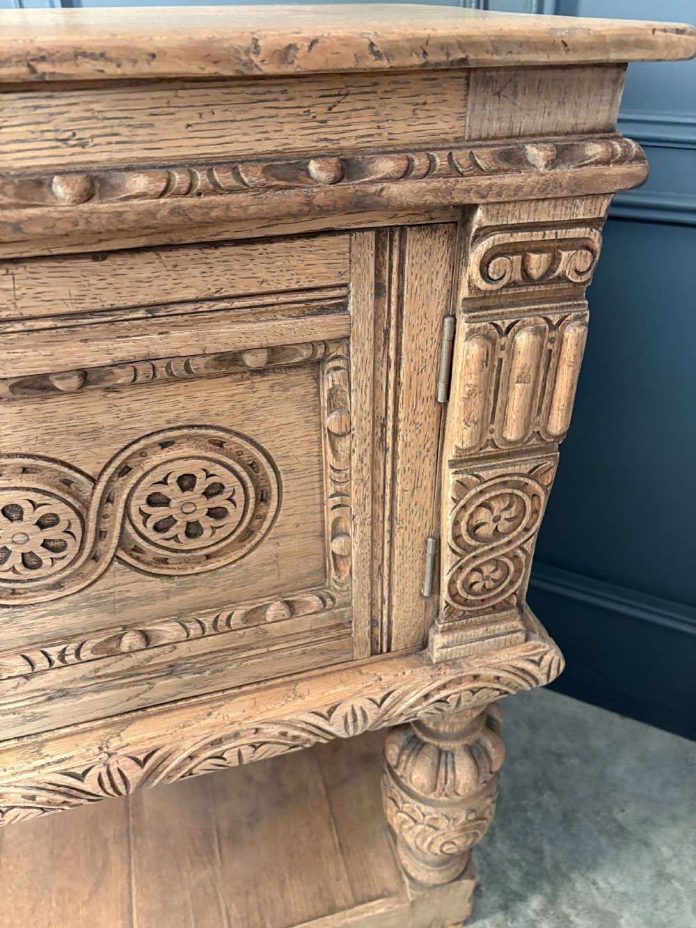 A carved bleached oak sideboard featuring geometric relief panel doors, central drawers, turned front legs, and an open lower pot board shelf. View III