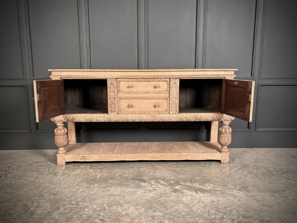 A carved bleached oak sideboard featuring geometric relief panel doors, central drawers, turned front legs, and an open lower pot board shelf. View IX