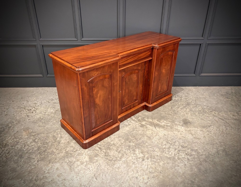 A Victorian mahogany three-door sideboard featuring flame mahogany panelled cupboard doors and a central top drawer on a solid plinth base.
