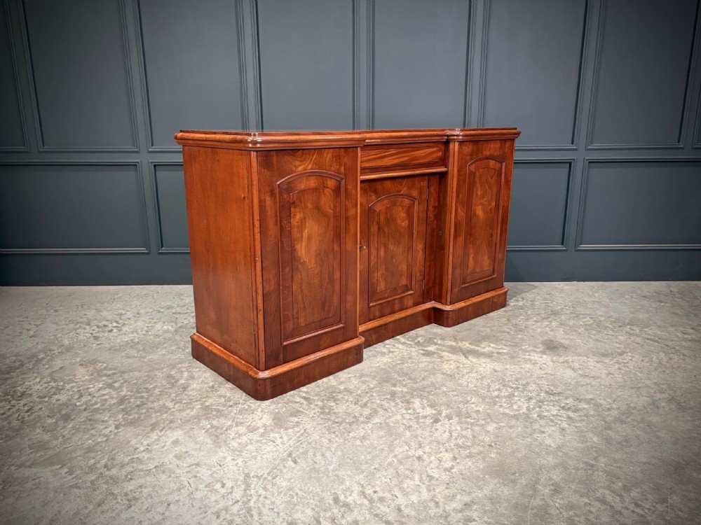 A Victorian mahogany three-door sideboard featuring flame mahogany panelled cupboard doors and a central top drawer on a solid plinth base. View II