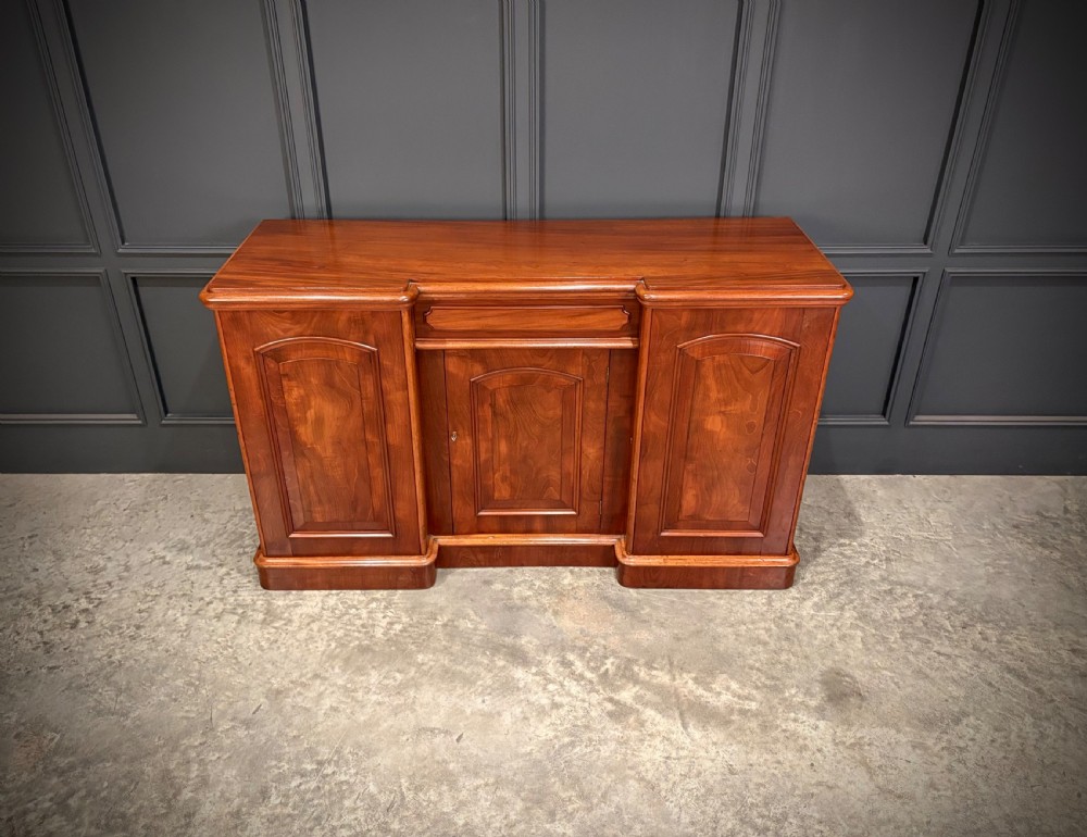 A Victorian mahogany three-door sideboard featuring flame mahogany panelled cupboard doors and a central top drawer on a solid plinth base. View III
