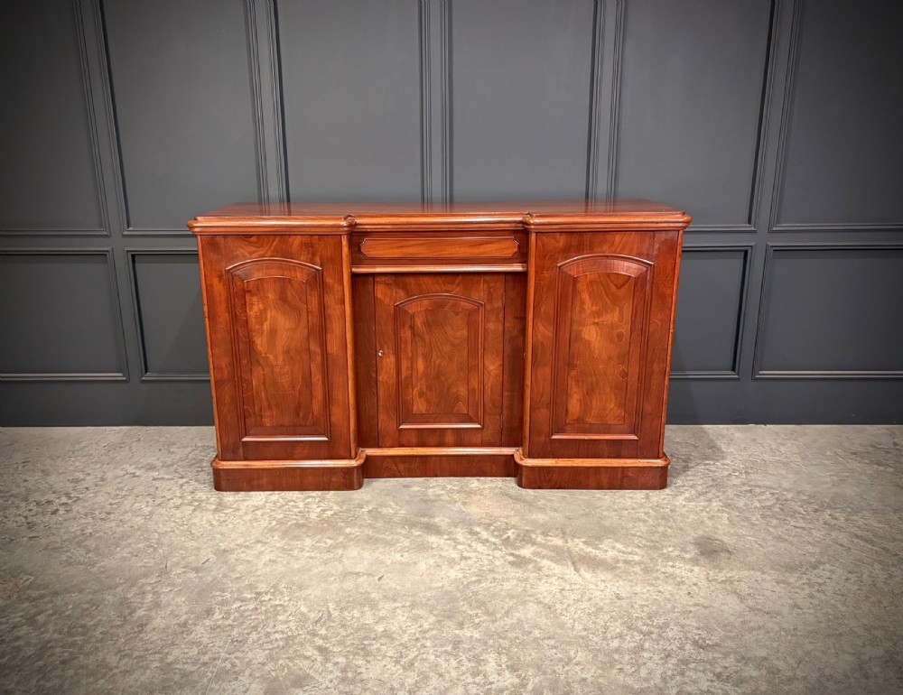 A Victorian mahogany three-door sideboard featuring flame mahogany panelled cupboard doors and a central top drawer on a solid plinth base. View IV