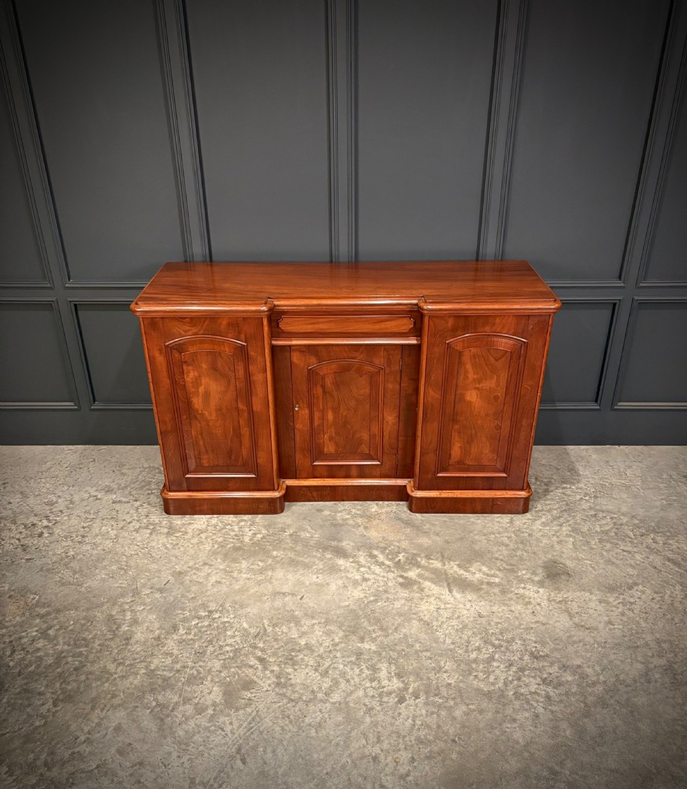 A Victorian mahogany three-door sideboard featuring flame mahogany panelled cupboard doors and a central top drawer on a solid plinth base. View V