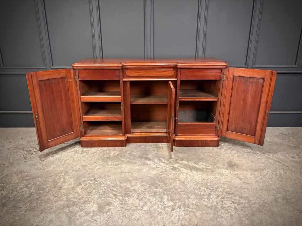 A Victorian mahogany three-door sideboard featuring flame mahogany panelled cupboard doors and a central top drawer on a solid plinth base. View VI