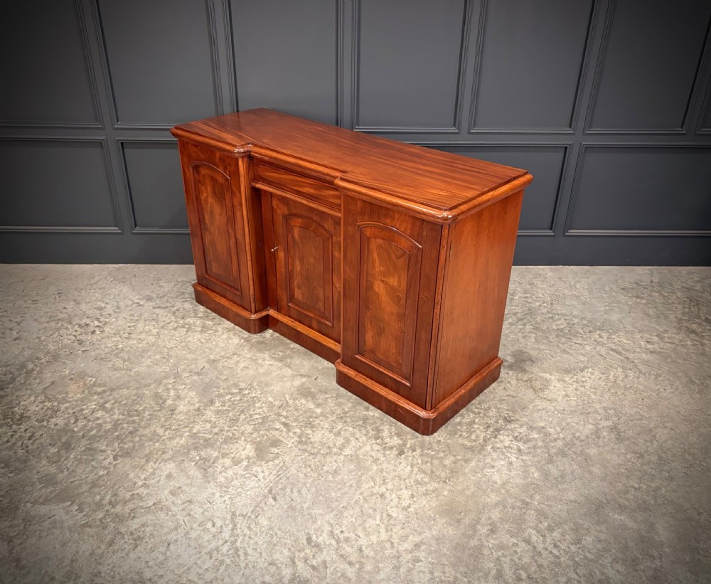 A Victorian mahogany three-door sideboard featuring flame mahogany panelled cupboard doors and a central top drawer on a solid plinth base. View VIII